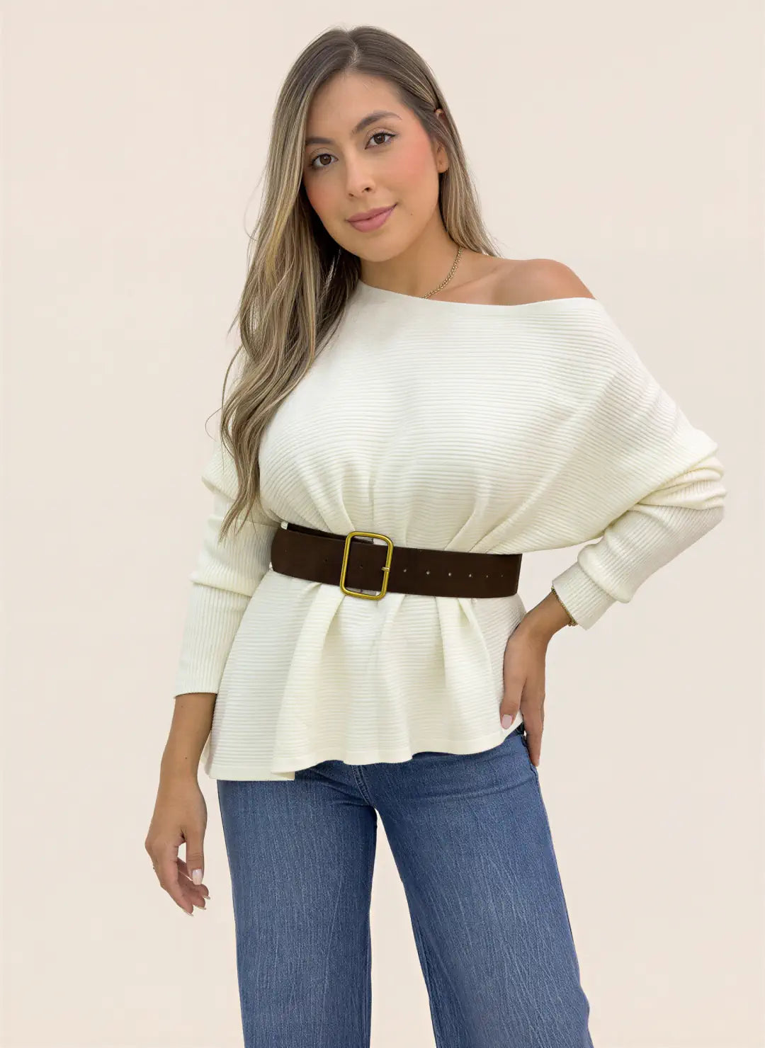 Mujer luciendo blusa tejida marfil de manga larga, escote amplio y textura acanalada, combinada con jeans.