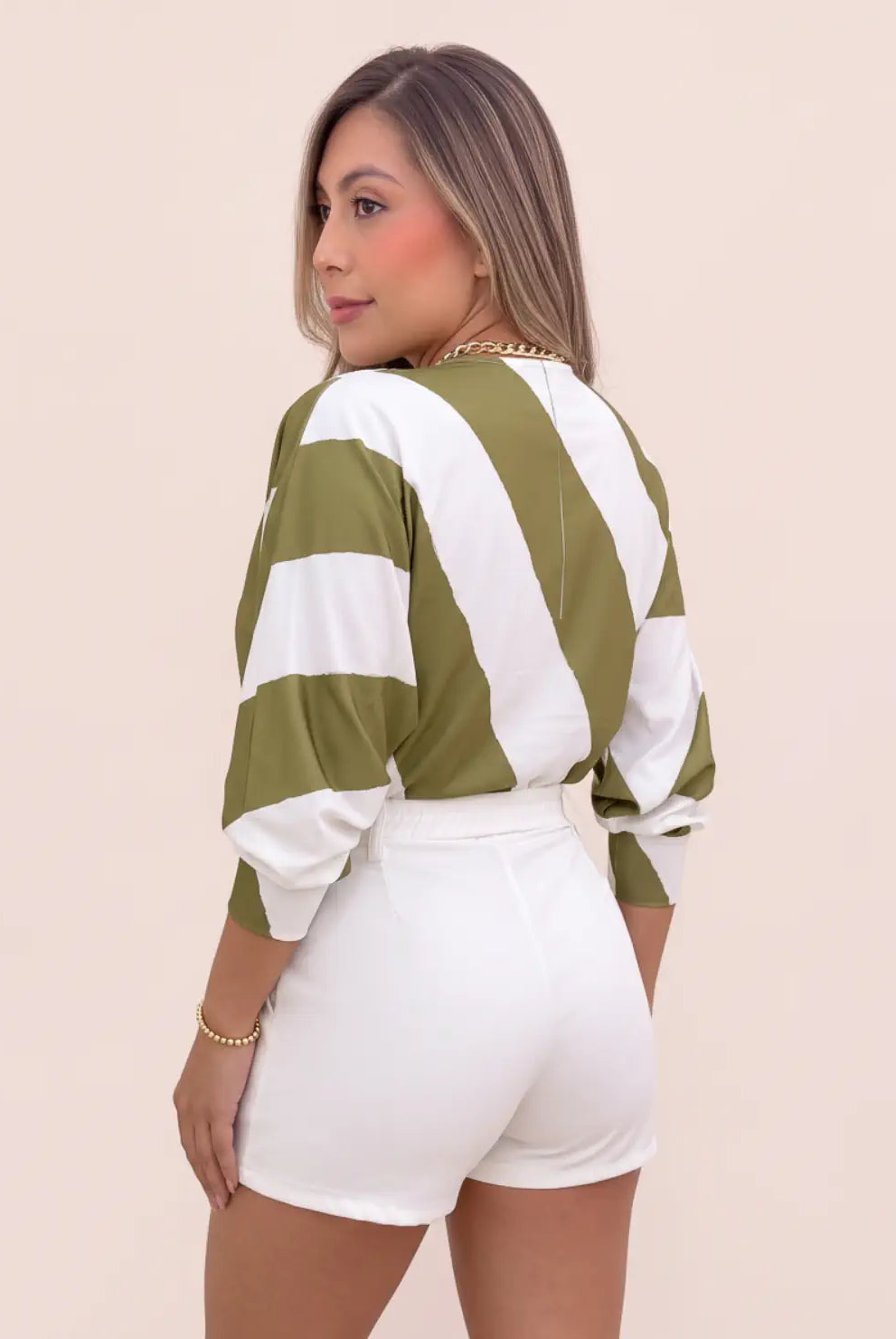 Vista posterior de blusa estampada verde oliva y blanca para mujer, con líneas anchas, mangas amplias y puños ajustados, combinada con short blanco.