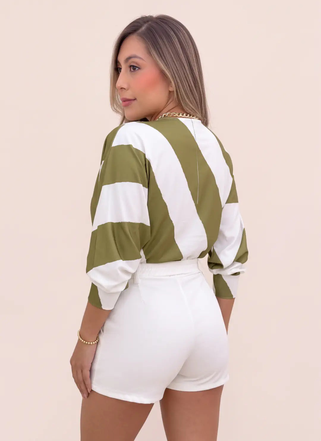 Vista posterior de blusa estampada verde oliva y blanca para mujer, con líneas anchas, mangas amplias y puños ajustados, combinada con short blanco.