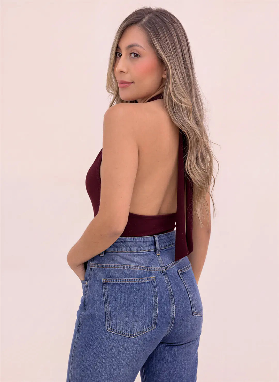 Blusa vinotinto para mujer de cuello halter con espalda descubierta y tiras largas que caen por detrás, combinada con jean azul.