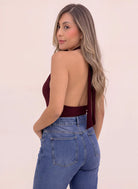 Blusa vinotinto para mujer de cuello halter con espalda descubierta y tiras largas que caen por detrás, combinada con jean azul.