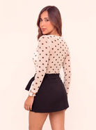 Vista posterior de falda short negra de tiro alto con cinturón ajustable, combinada con body blanco de lunares negros.