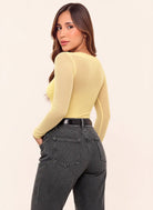 Vista posterior de body amarillo pastel para mujer con mangas largas en mesh transparente y espalda semitransparente, combinado con jean gris.