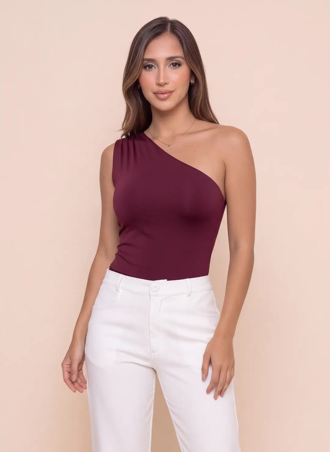 Modelo luciendo body Vinotinto de un solo hombro con escote asimétrico y diseño ajustado, combinado con pantalón blanco de mujer.